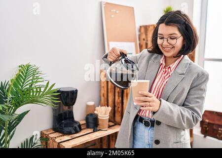 Junge Frau, die im Büro Kaffee auf Glas schüttet Stockfoto