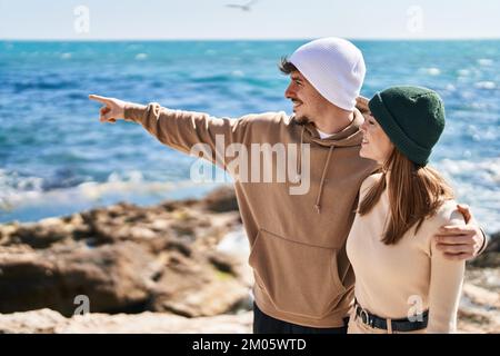Ein Paar aus Mand und Frau umarmt sich, zeigt mit dem Finger auf das Meer Stockfoto