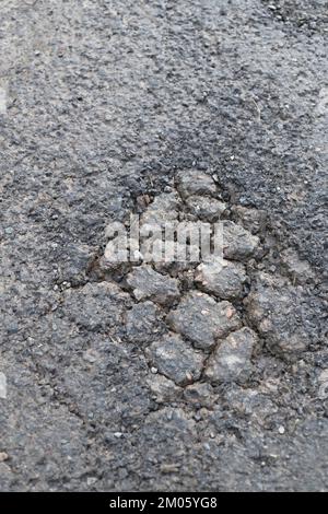 Oberer Asphaltbelag verschlissen mit nachfolgender Ermüdung und Alligatorrissen entwickeln sich zu einem Schlagloch. Für schlecht instand gehaltene Straßen. Stockfoto