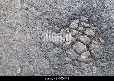 Oberer Asphaltbelag verschlissen mit nachfolgender Ermüdung und Alligatorrissen entwickeln sich zu einem Schlagloch. Für schlecht instand gehaltene Straßen. Stockfoto