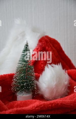 Weihnachtsdekorationen. Ein kleiner künstlicher Weihnachtsbaum mit künstlichem Schnee auf einem roten Weihnachtsmann-Hut. Stockfoto