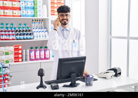 Junger hispanischer Apotheker, der auf dem Smartphone spricht und in der Apotheke arbeitet Stockfoto