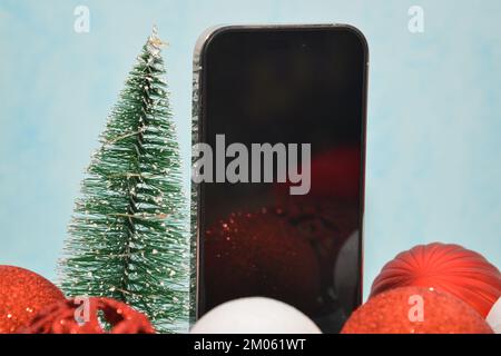 Riga/Lettland – 4. Dezember 2022: Neues modernes Telefon – schwarzer Bildschirm für iPhone 14 pro. Glitzernde Weihnachtsdekorationen auf blauem Hintergrund. Weihnachtsgeschenk Konz Stockfoto