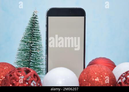 Riga/Lettland – 4. Dezember 2022: Neues modernes Telefon – weißer Bildschirm des iPhone 14 pro. Glitzernde Weihnachtsdekorationen auf blauem Hintergrund. Weihnachtsgeschenk Konz Stockfoto