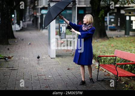 Eine Frau öffnet einen Schirm auf der Straße in der Stadt. Stockfoto