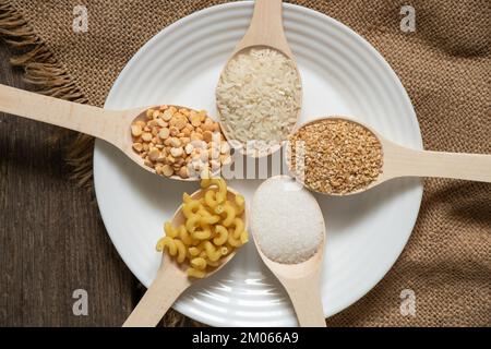 Zucker, Reiserbsen, Pasta, Müsli auf Holzlöffeln auf dem Tisch in der Küche, Essen Stockfoto