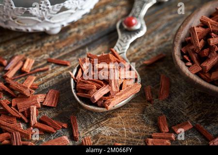 Rote Sandelholzstücke auf einem Löffel auf einem Holztisch. Zutat zur Herstellung ätherischer Öle. Stockfoto