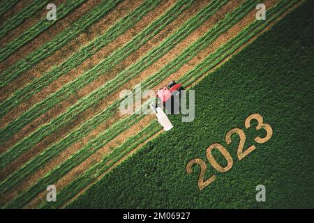 2023 ein gutes Neujahrskonzept für Landwirtschaft, Unternehmen, Ziele, Erfolg und Neubeginn. Industrietraktor auf einem grünen Feld. Stockfoto