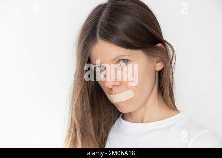 Ein Mädchen, das seinen Mund mit Klebeband über isoliertem Hintergrund versiegelt hat, sei still und sag nichts, geheim Stockfoto