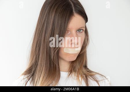 Ein Mädchen, das seinen Mund mit Klebeband über isoliertem Hintergrund versiegelt hat, sei still und sag nichts, geheim Stockfoto