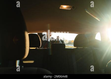 Aus dem Inneren des Wagens, ein lächelnder Mann, der Dinge aus dem Kofferraum des Wagens nahm Stockfoto