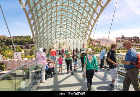 Tiflis, Georgia - 07 23 2022: Touristen auf der stilvollen, modernen Friedensbrücke, die über den Fluss Mtkvari Kura in der Hauptstadt von Georgia Tiflis errichtet wurde Stockfoto