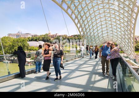 Tiflis, Georgia - 07 23 2022: Touristen auf der stilvollen, modernen Friedensbrücke, die über den Fluss Mtkvari Kura in der Hauptstadt von Georgia Tiflis errichtet wurde Stockfoto