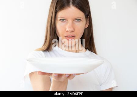 Das Mädchen hält einen leeren weißen Teller auf weißem Hintergrund, der Kellner mit einem Teller Stockfoto