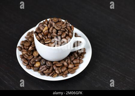 Kaffeebohnen in weißer Tasse auf dunklem Holztisch. Dunkler und gerösteter Kaffee, Konzept eines natürlichen Getränks Stockfoto