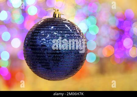 Weihnachtsspielzeug, blauer, glänzender Ball auf verschwommenem weihnachtlichem Hintergrund. Neujahrsdekoration Stockfoto