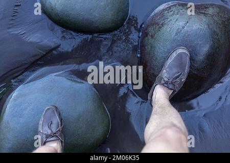 Männerfüße in den oberen Sidern auf grünen Steinen über Wasser Stockfoto