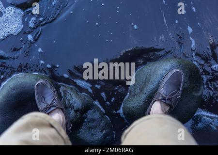 Männerfüße in den oberen Sidern auf grünen Steinen über Wasser Stockfoto