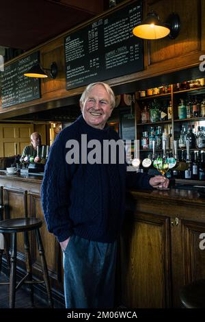 Ein glücklicher Mann stand an der Bar und trank ein Glas Wein. Das Gunton Arms, North Norfolk, England Stockfoto