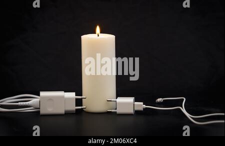 Blackout-Konzept. Ladegerät mit Kabel in der Nähe der Kerze auf dunklem Hintergrund. Stockfoto