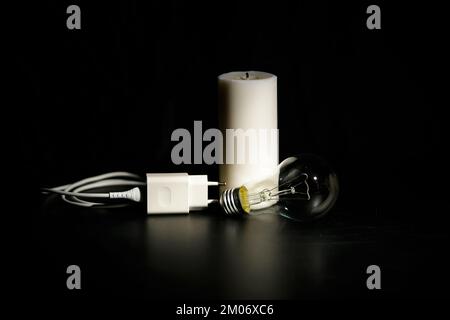 Blackout-Konzept. Ladegerät mit Kabel in der Nähe der Kerze auf dunklem Hintergrund. Stockfoto