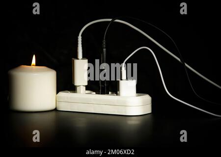 Blackout-Konzept. Ladegerät mit Kabel in der Nähe der Kerze auf dunklem Hintergrund. Stockfoto