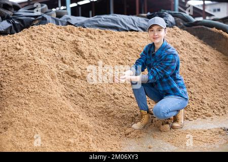 Eine Farmerin, die auf einem großen Haufen abgebrannter Körner der Brauerei hockt Stockfoto