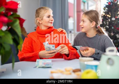 Mutter gibt der Teenager-Tochter Geld, um weihnachten und Neujahr zu feiern Stockfoto