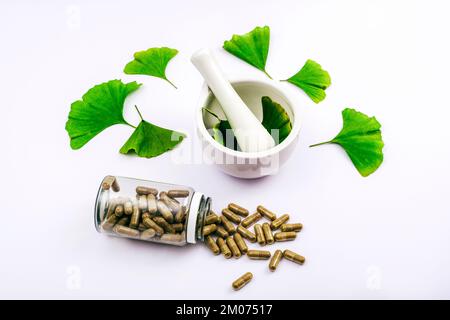 Pillen und frische grüne Ginkgo-biloba-Blätter, Mörtel und Stößel auf weißem Hintergrund. Naturheilkräutermedizinisches Konzept. Draufsicht. Stockfoto