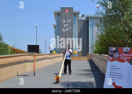 Alphorn-Spieler in seinem traditionellen Kostüm steht und spielt Musik am Eingang des Schweizer Pavillons auf der EXPO Milano 2015 - beste Einladung. Stockfoto