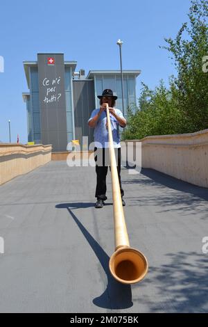 Alphorn-Spieler in seinem traditionellen Kostüm steht und spielt Musik am Eingang des Schweizer Pavillons auf der EXPO Milano 2015 - beste Einladung. Stockfoto