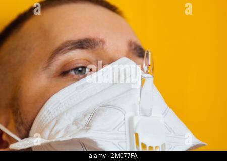 Porträt eines jungen Arztes in einem Beatmungsgerät auf gelbem Hintergrund. Respiratorische Coronavirus-Impfstoffampullen. Sehen Sie sich die Ampulle an. Der Erfinder von Th Stockfoto