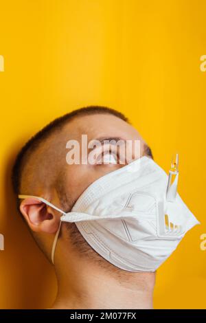 Porträt eines jungen Arztes in einem Beatmungsgerät auf gelbem Hintergrund. Respiratorische Coronavirus-Impfstoffampullen. Sehen Sie sich die Ampulle an. Der Erfinder von Th Stockfoto