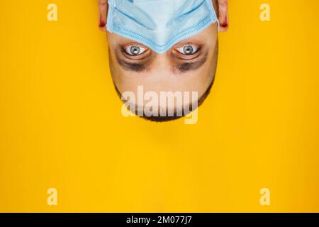 Nahaufnahme Porträt eines attraktiven jungen Mannes rollte seine Augen mit einer Schutzmaske auf seinem Gesicht. Angst, krank zu werden, Coronavirus-Konzept. Ohne Schüler Stockfoto