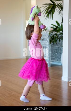 Zwei Jahre altes Mädchen, das ihr Stoffspielzeug über den Kopf hielt Stockfoto