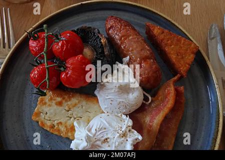 Gutes warmes britisches Frühstück, pochierte Eier, Halloumi, Speck, Würstchen, Haschbraun, auf Tomaten und Pilzen gebraten Stockfoto