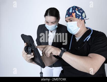 Der Arzt zeigt dem Patienten eine Tablette, trägt beide Masken und weist auf den Inhalt hin, den er zeigt, oder erklärt ihn. Stockfoto