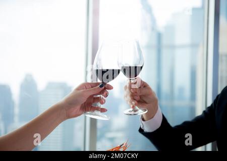 Die Hände eines jungen Paares, das sich mit einem Glas Wein in der Hand hält, jubeln im Restaurant zum Feiern zusammen, Mann und Frau treffen sich mit Romantikern und Narren Stockfoto
