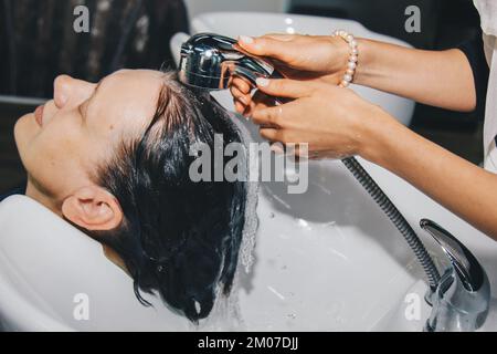 Eine wunderschöne, fröhliche ältere Frau genießt eine Kopfmassage, während sie sich von einem professionellen Friseur die Haare wäscht. Schönheitspflege, Frisur, Mode, Lifestyle Stockfoto