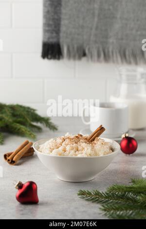 Skandinavischer Reisbrei mit Zimt in einer Schüssel, umgeben von Weihnachtskugeln. Frühstück am Heiligabend. Stockfoto