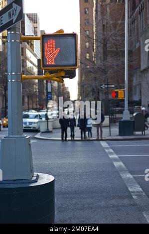 Metallstange an einer Ecke in New york mit einem roten handbeleuchteten Schild, dass die Straße nicht überquert werden darf, mit verschwommenen Menschen im Hintergrund Stockfoto