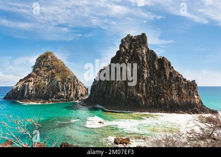 Blick vom Morro Dois São in Fernando de Noronha, mit klarer Sonne, spärlichen Wolken, blauem und türkisfarbenem kristallklarem Wasser und weißem Schaum von den Wellen Stockfoto