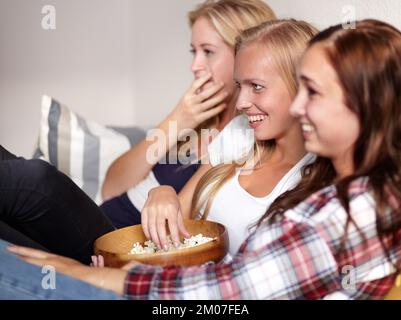 Popcorn und ein Film. Drei junge Freunde genießen eine Schüssel Popcorn, während sie sich einen Film ansehen. Stockfoto