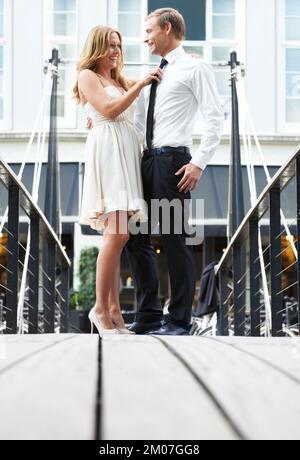 Verspieltes Paar. Eine schöne Frau steht mit ihrem Freund auf einer Brücke und spielt mit seiner Krawatte. Stockfoto