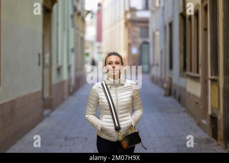 Eine attraktive Frau mittleren Alters mit blonden Haaren und einem Pferdeschwanz, die eine metallische Jacke trägt und eine Handtasche über der Schulter trägt, geht nach unten Stockfoto