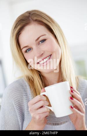 Sie mag eine erfrischende Tasse Tee. Süße junge Frau, die eine Tasse Kaffee mit einem Lächeln trinkt. Stockfoto