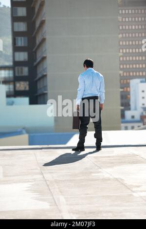 Die schwerste Entscheidung meines Lebens. Rückblick auf einen Geschäftsmann, der seine Aktentasche am Rand eines Dachs hält. Stockfoto