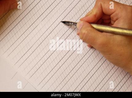 Weibliche Hand schreibt mit dem Tintenstift auf leeres weißes Papierblatt mit Streifen. Schreibwaren auf dem Schreibtisch aus nächster Nähe. Rechtschreibunterricht und Caligraphie Ex Stockfoto