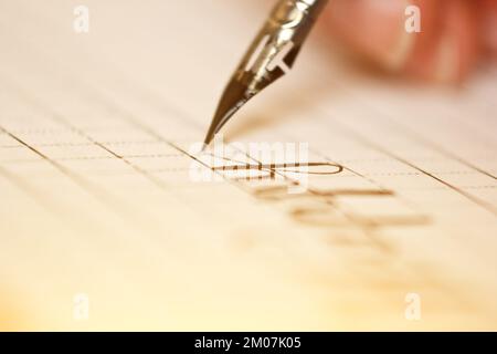 Weibliche Hand schreibt mit dem Tintenstift auf einem weißen Papierbogen mit Streifen. Schreibwaren auf dem Schreibtisch aus nächster Nähe. Rechtschreibunterricht und Caligraphie-Übungen Stockfoto