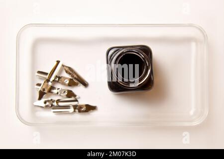 Tintenflasche mit Metallspitzen für Tintenstift auf weißem Hintergrund. Schreibwaren auf weißem Schreibtisch, Nahansicht von oben. Rechtschreibunterricht und Caligraphie-Übungen. T Stockfoto
